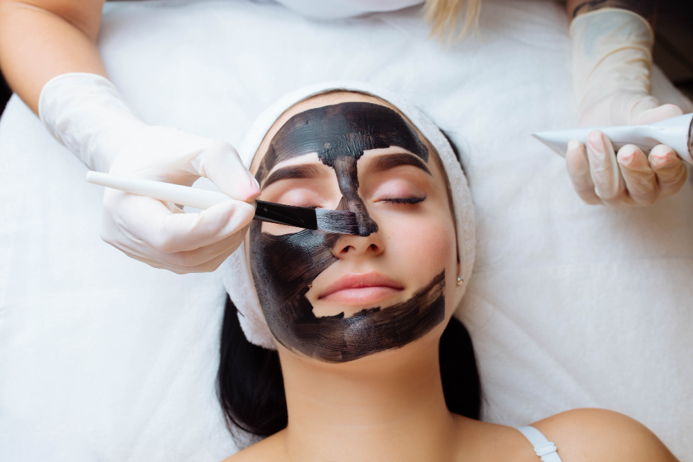 cosmetologist applying black mask pretty woman face wearing black gloves gorgeous woman spa